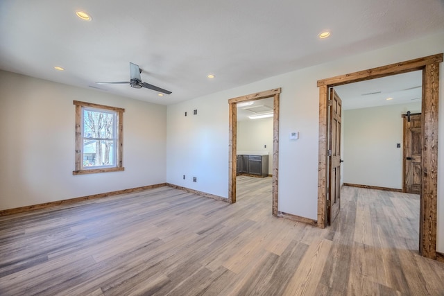 unfurnished room featuring light wood-style floors, a ceiling fan, baseboards, and a barn door