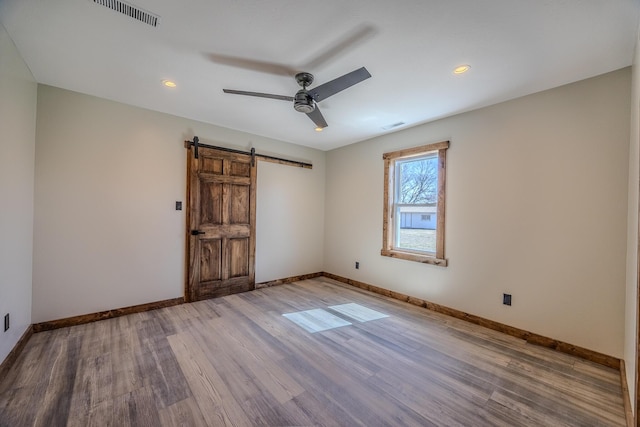 spare room with a barn door, baseboards, visible vents, a ceiling fan, and wood finished floors