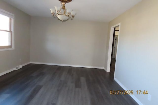 empty room featuring a chandelier, visible vents, baseboards, and wood finished floors