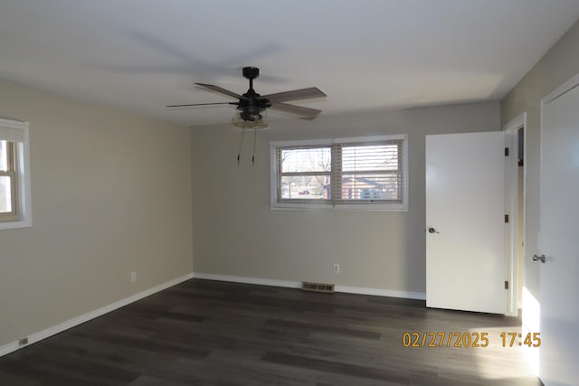 empty room featuring visible vents, a ceiling fan, dark wood-type flooring, and baseboards