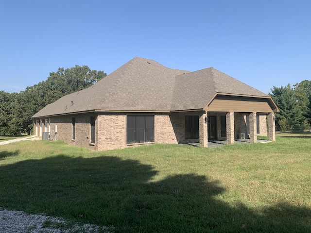 rear view of house featuring brick siding, roof with shingles, and a yard