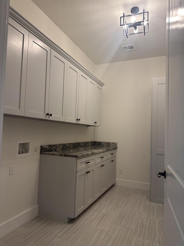 laundry area with washer hookup, cabinet space, visible vents, a textured ceiling, and baseboards