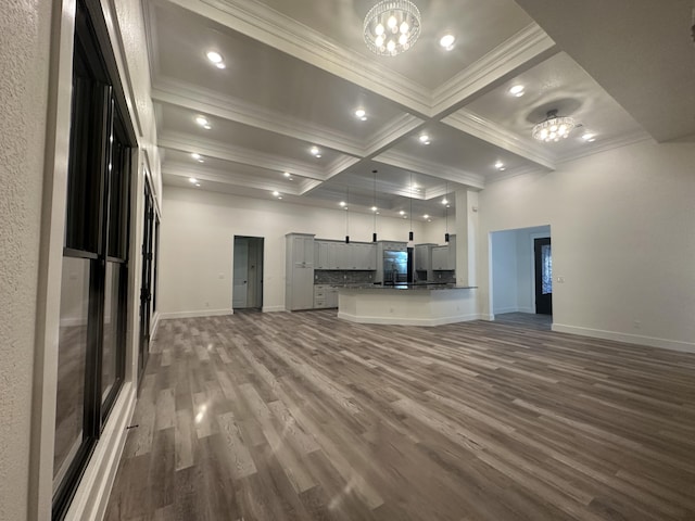 unfurnished living room with coffered ceiling, dark wood finished floors, ornamental molding, beamed ceiling, and a notable chandelier