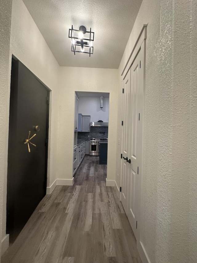 hall featuring baseboards, dark wood finished floors, a textured ceiling, and a textured wall