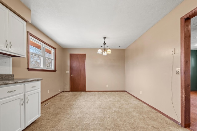 kitchen with dark countertops, light colored carpet, white cabinetry, and baseboards