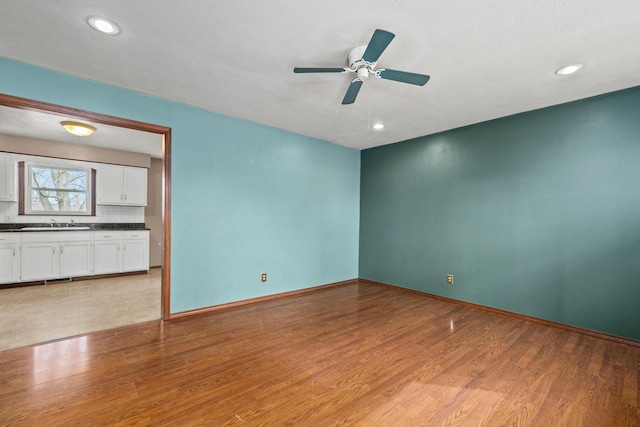 empty room featuring recessed lighting, baseboards, light wood-type flooring, and a sink