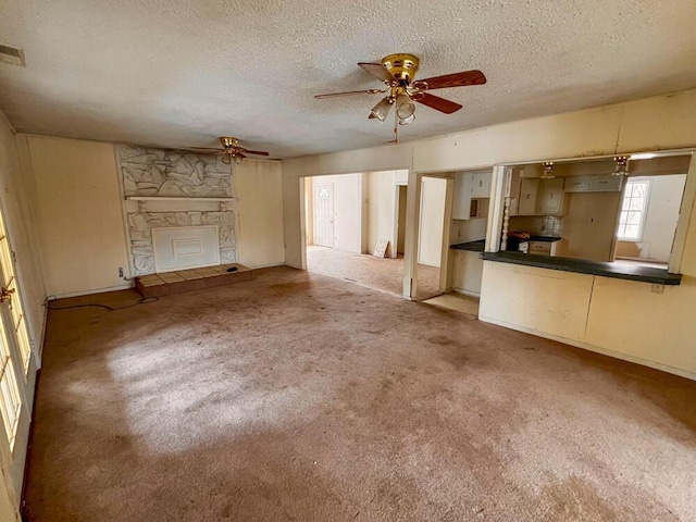 unfurnished living room with visible vents, a textured ceiling, carpet floors, a fireplace, and ceiling fan