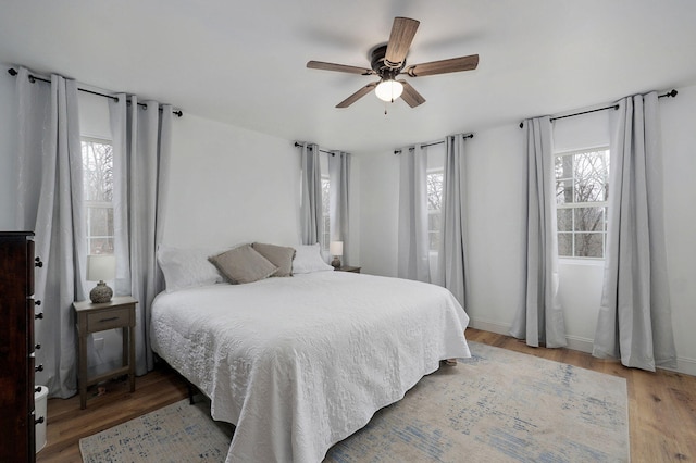 bedroom with multiple windows, a ceiling fan, baseboards, and light wood finished floors