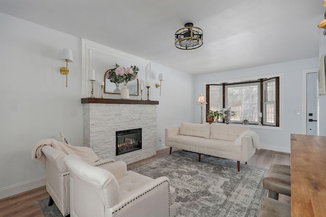 living room with a stone fireplace, baseboards, and wood finished floors