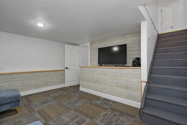 living room featuring a wainscoted wall, dark carpet, baseboards, and stairs