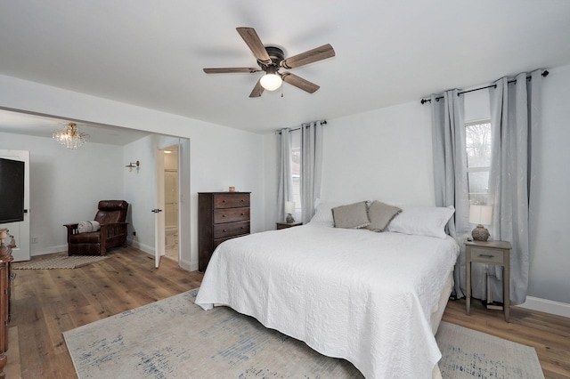 bedroom with baseboards, wood finished floors, and ceiling fan with notable chandelier