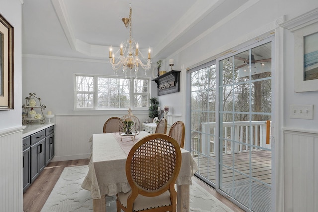 dining area featuring a notable chandelier, a wainscoted wall, a raised ceiling, and light wood-style floors