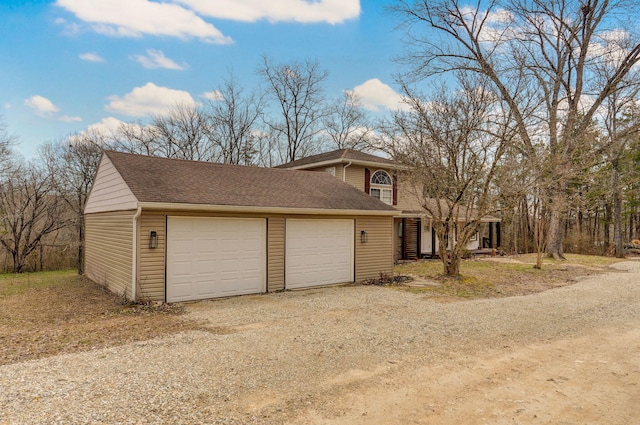 view of front of house featuring a garage, dirt driveway, and a shingled roof