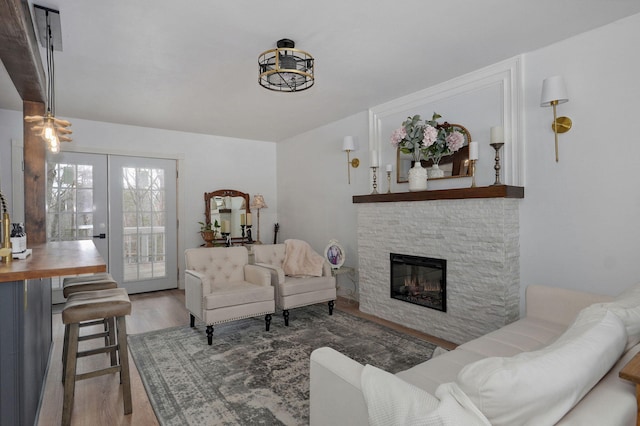 living room with a stone fireplace, wood finished floors, and french doors