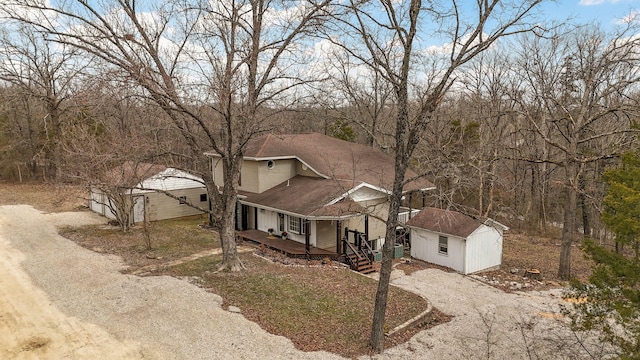 view of front of home with an outbuilding, a storage unit, dirt driveway, and a shingled roof