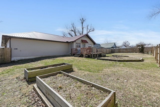 exterior space featuring a front yard, a vegetable garden, a fenced backyard, a deck, and metal roof