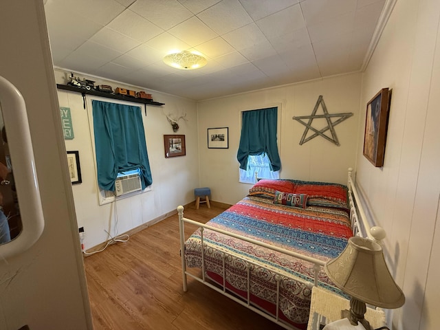 bedroom with cooling unit, wood finished floors, baseboards, and ornamental molding