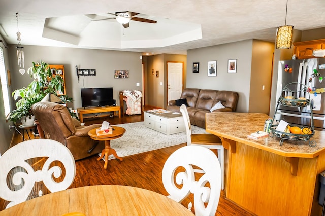 living room with a raised ceiling, ceiling fan, and dark wood-style flooring