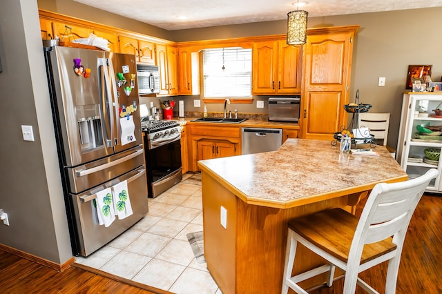 kitchen featuring a kitchen island, light countertops, appliances with stainless steel finishes, light tile patterned flooring, and a sink