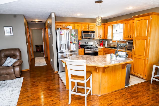 kitchen featuring a sink, stainless steel appliances, light wood-style floors, a kitchen bar, and brown cabinets