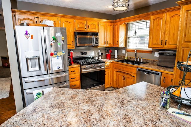 kitchen with brown cabinetry, appliances with stainless steel finishes, tile counters, and a sink