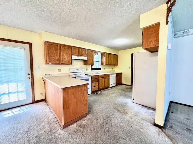 kitchen featuring under cabinet range hood, light carpet, a peninsula, brown cabinetry, and white appliances