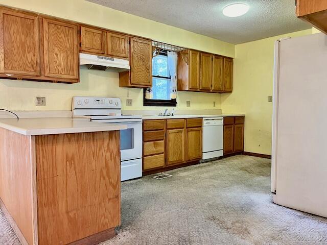 kitchen with under cabinet range hood, brown cabinets, white appliances, and light countertops