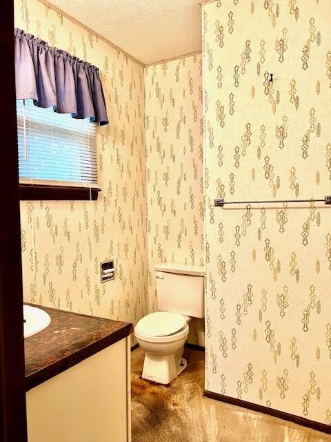 bathroom featuring a textured ceiling, toilet, vanity, and wallpapered walls