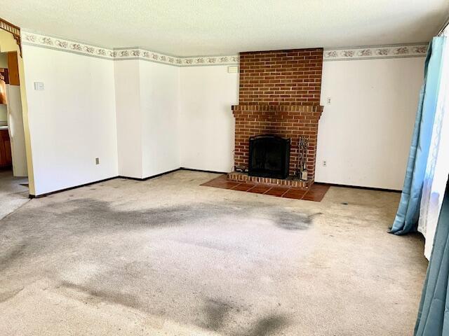 unfurnished living room with baseboards, carpet floors, a textured ceiling, and a fireplace