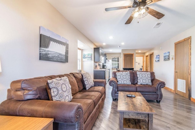 living area featuring baseboards, visible vents, light wood finished floors, and ceiling fan