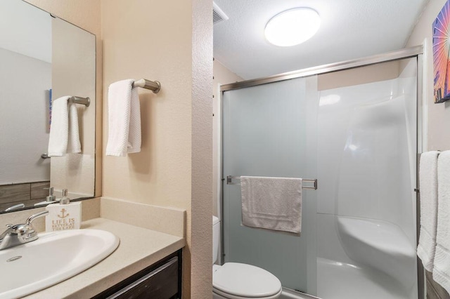 bathroom featuring visible vents, toilet, a stall shower, vanity, and a textured wall