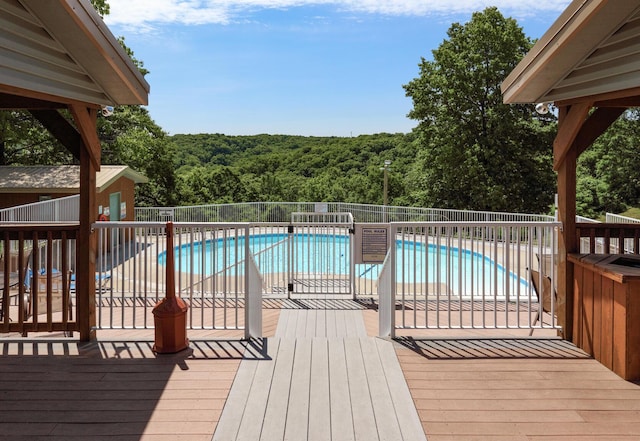 wooden terrace with a fenced in pool and a view of trees