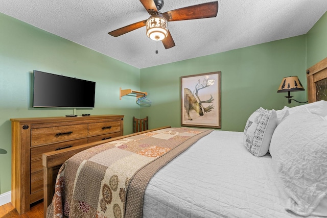 bedroom with ceiling fan, wood finished floors, and a textured ceiling