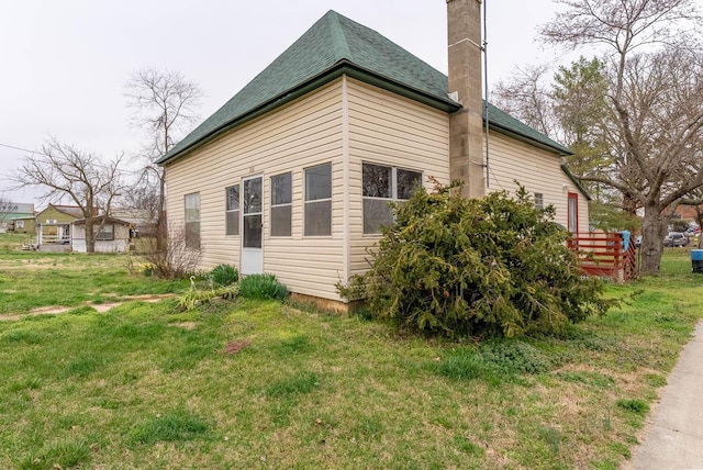 view of home's exterior with a yard, roof with shingles, and a chimney