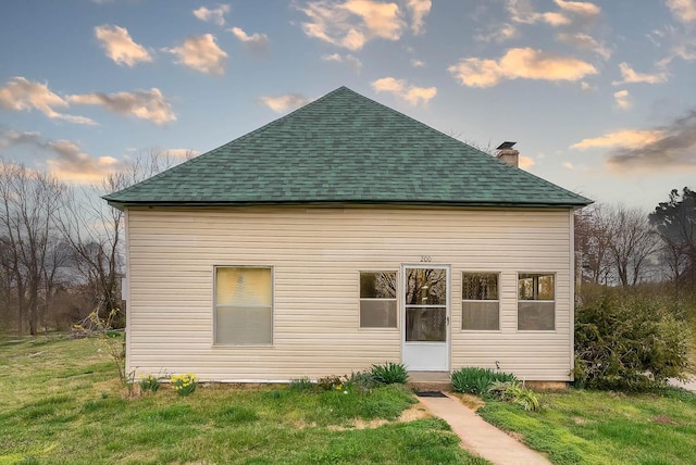 back of house featuring a lawn, roof with shingles, and a chimney