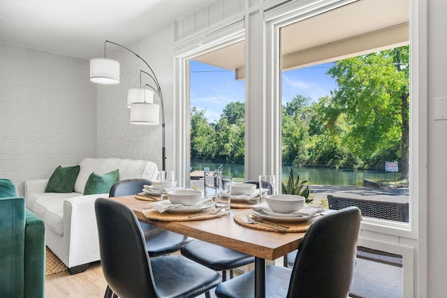 dining space featuring a water view, light wood-style floors, and brick wall