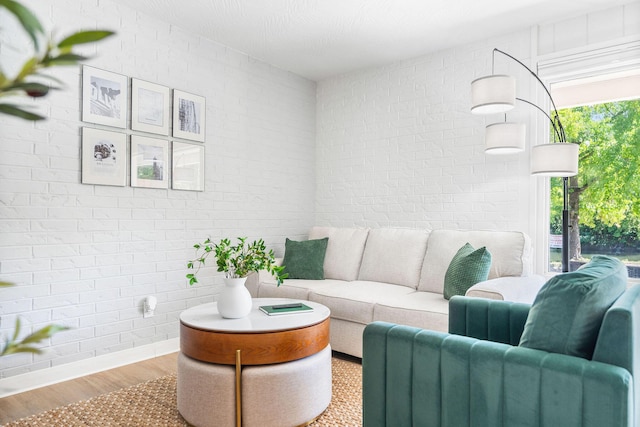 living area with brick wall, baseboards, and wood finished floors