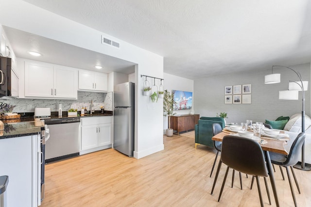 kitchen with light wood finished floors, visible vents, dishwashing machine, freestanding refrigerator, and a sink