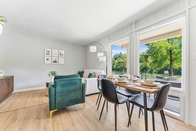 dining space featuring light wood-style floors and brick wall