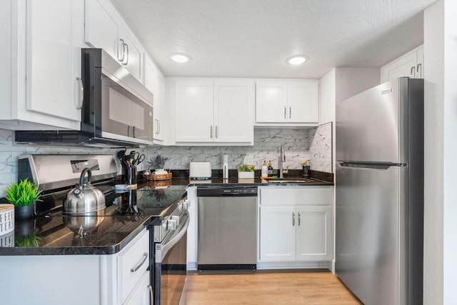 kitchen featuring a sink, appliances with stainless steel finishes, white cabinetry, dark countertops, and backsplash