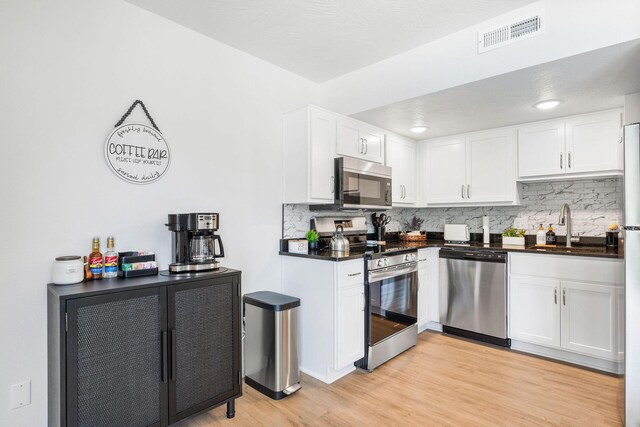 kitchen with dark countertops, visible vents, light wood-style floors, stainless steel appliances, and a sink