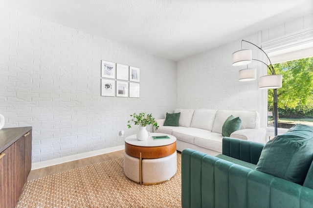 living area with brick wall and wood finished floors