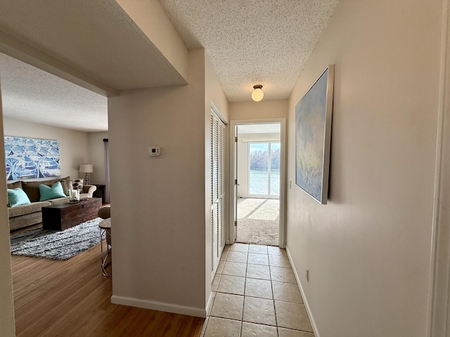 hall with baseboards, a textured ceiling, and light wood-style flooring