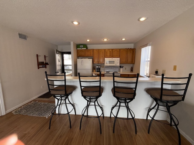 kitchen with visible vents, white appliances, dark wood finished floors, and a kitchen breakfast bar