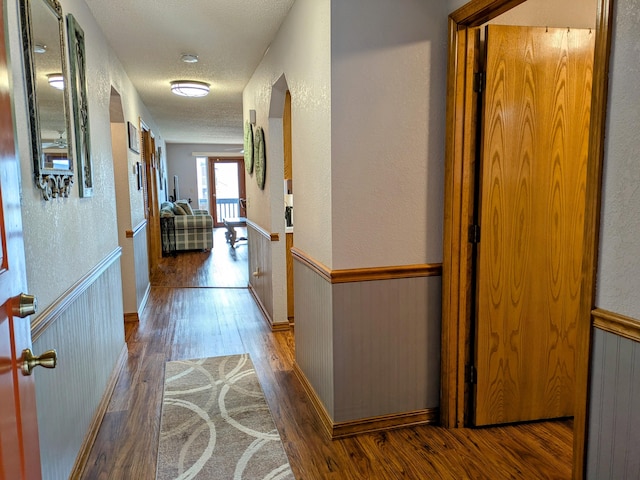 corridor featuring a wainscoted wall, a textured ceiling, a textured wall, and wood finished floors