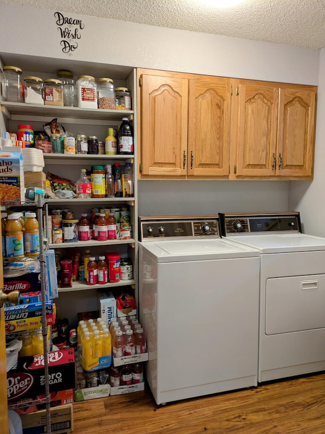 clothes washing area with cabinet space, a textured ceiling, wood finished floors, and separate washer and dryer