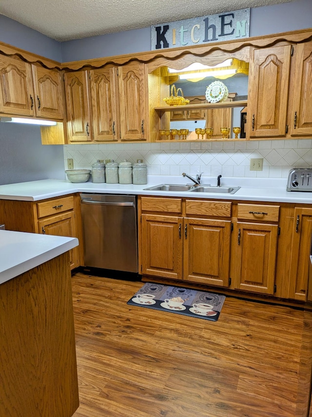 kitchen with wood finished floors, a sink, light countertops, a textured ceiling, and stainless steel dishwasher