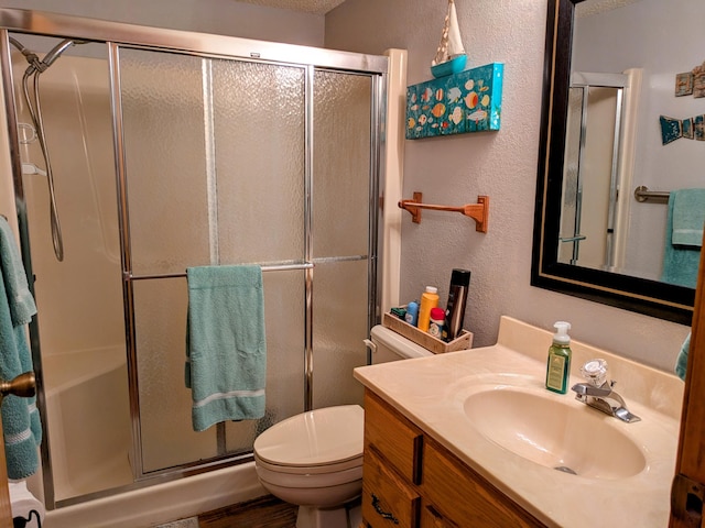 bathroom featuring vanity, a shower stall, toilet, and a textured wall