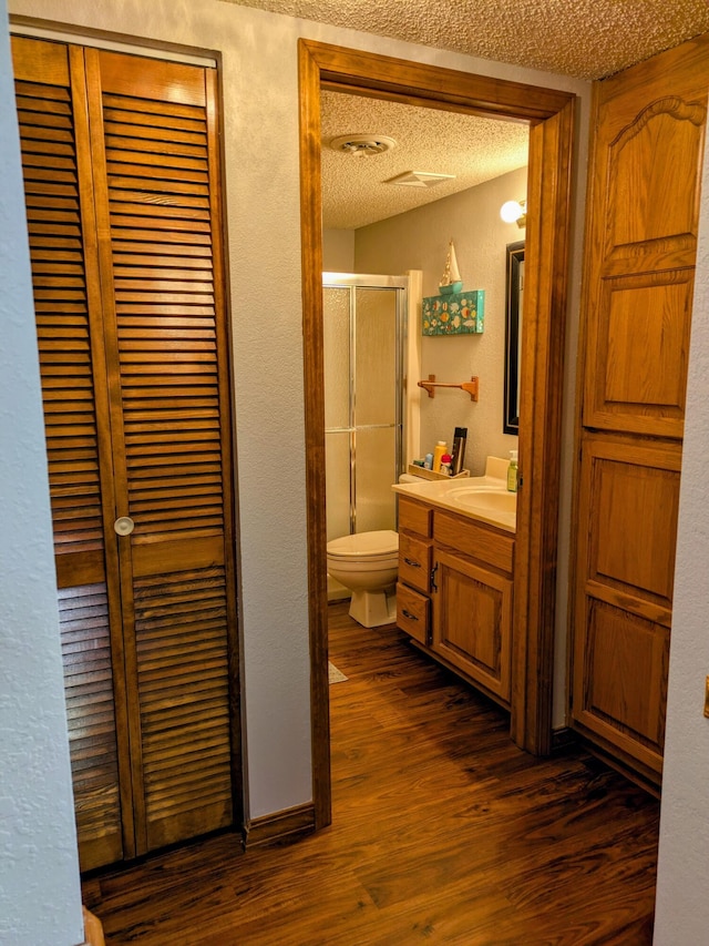 bathroom with toilet, a textured ceiling, wood finished floors, a shower stall, and vanity