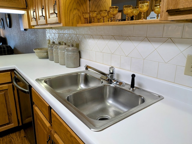 kitchen featuring brown cabinetry, a sink, light countertops, dishwasher, and backsplash